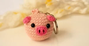 Chaveiro de porquinho feito em crochê estilo amigurumi com focinho rosa e olhos pretos, ideal para receita gratuita passo a passo.