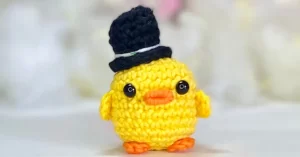 Pato amigurumi amarelo com cartola azul feita em crochê, ideal para ilustrar a receita passo a passo completa de chaveiro artesanal.