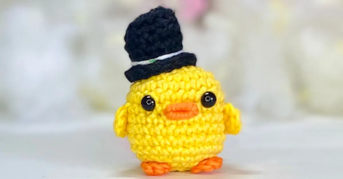 Pato amigurumi amarelo com cartola azul feita em crochê, ideal para ilustrar a receita passo a passo completa de amigurumi artesanal.