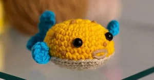 Peixe amigurumi colorido feito em crochê com barbante amarelo e barbante azul, ideal como chaveiro artesanal passo a passo.